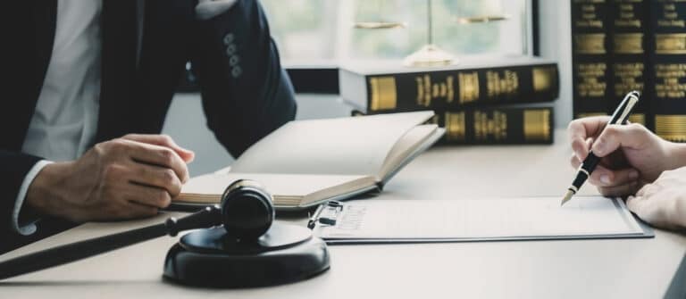 An auto accident lawyer discussing a case with their client. On their desk is paperwork, books, and a gavel.