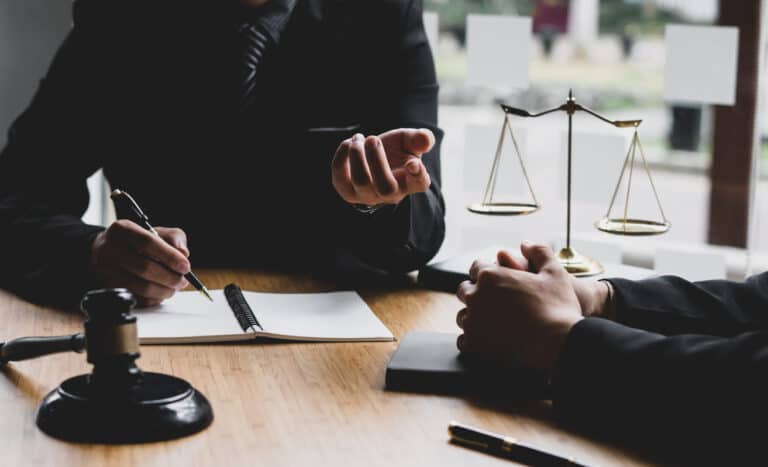 Two lawyers discussing a road rage incident. On their table is paperwork, a gavel, and the scales of justice.