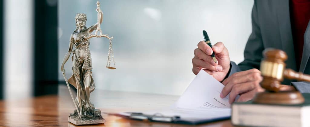 A bicycle accident attorney is working on paperwork at their desk. In front of them is a lady justice statue, a book and a gavel.