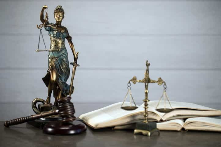 A lady justice statue, a gavel, and open book, and the scales of justice on a motorcycle accident injury attorney's desk.