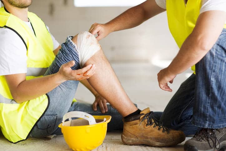 An employee helping another worker after they injured their knee on the job.