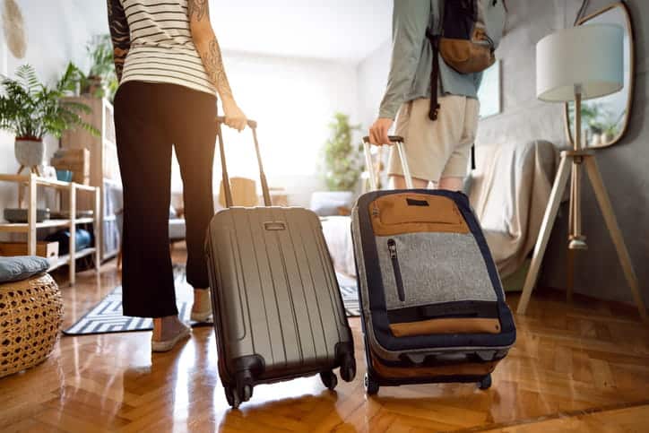 Two people wheeling suitcases walking into an Airbnb for a vacation stay.