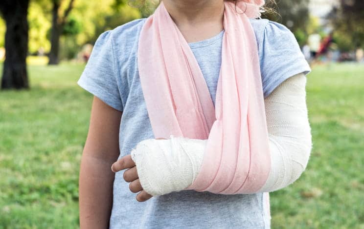 A child with a broken arm is in a cast and a pink sling.