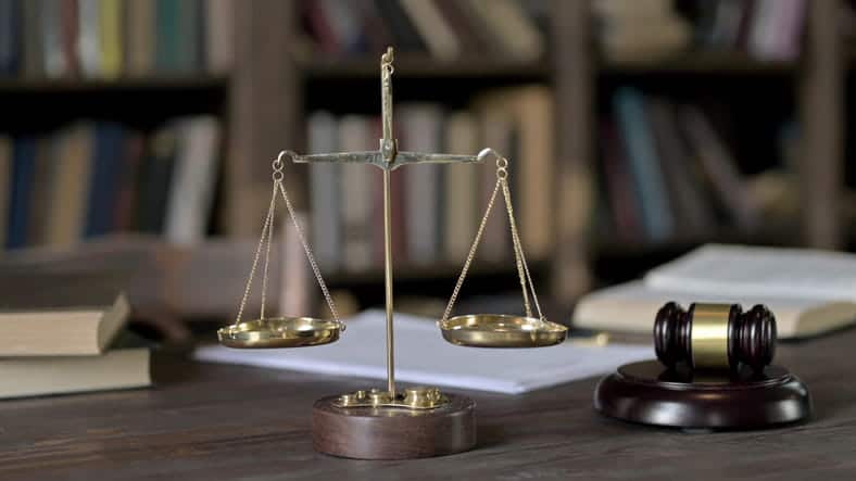 The scales of justice next to a gavel with law books in the background.