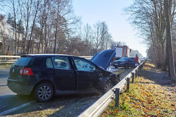 The scene of a car accident with a firetruck in the background. Two vehicles are damaged and on the side of the road.