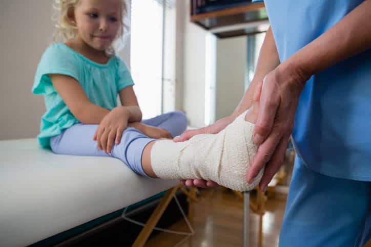 A little girl with her ankle wrapped as a school nurse inspects her injury.