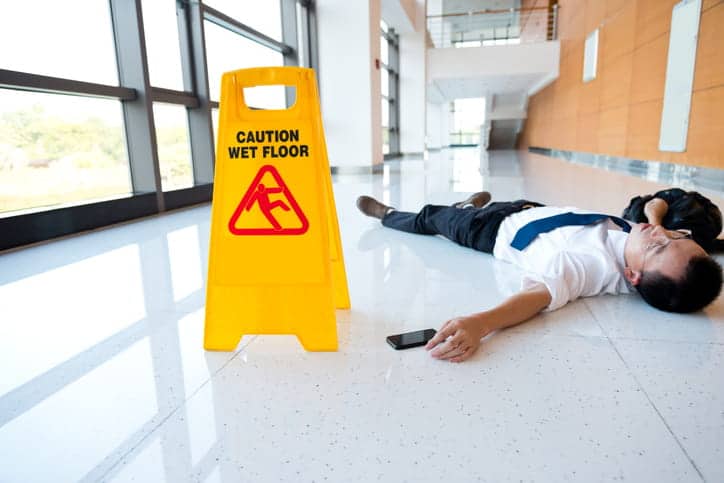 A man lying on the ground next to a yellow, caution: wet floor sign.