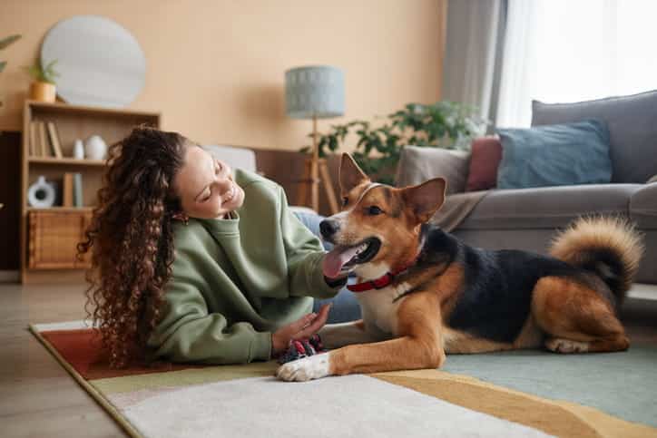 A woman lying on the floor of an airbnb smiling at her dog.