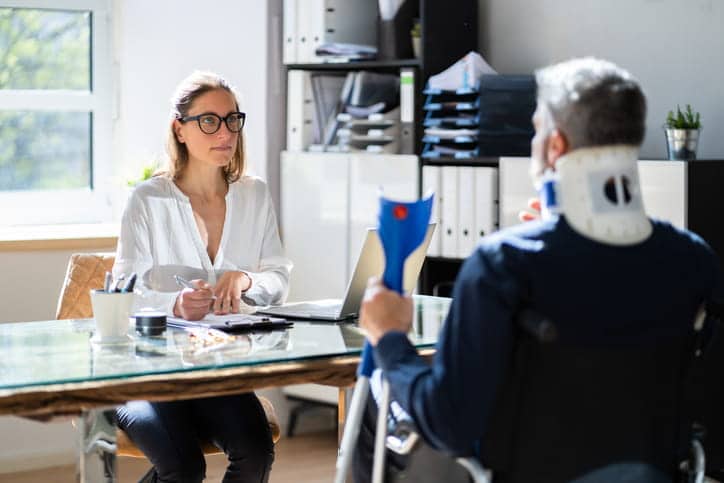 A personal injury attorney speaks with her client who sits in a wheelchair with a neck brace on.