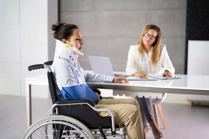 A woman in a neck brace, arm sling, and a wheelchair speaks with her personal injury attorney.