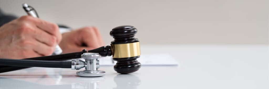 A lawyer filling out paperwork next to a gavel and a stethoscope.