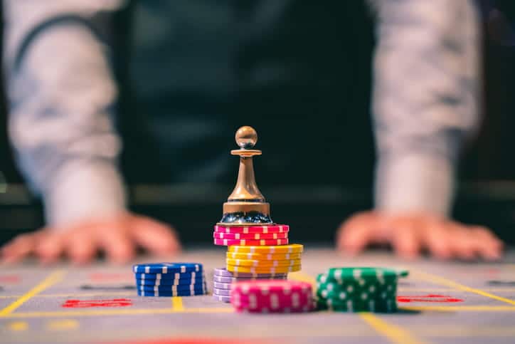 A dealer blurred out in the background as the focus remains on chips stacked on a game table in a casino.